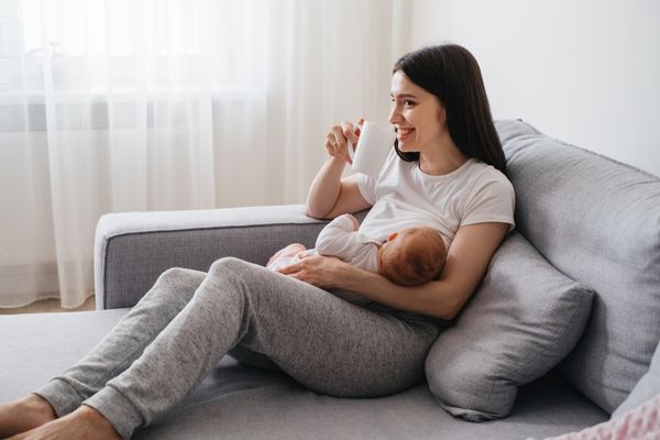 mom breastfeeding and drinking from a white cup